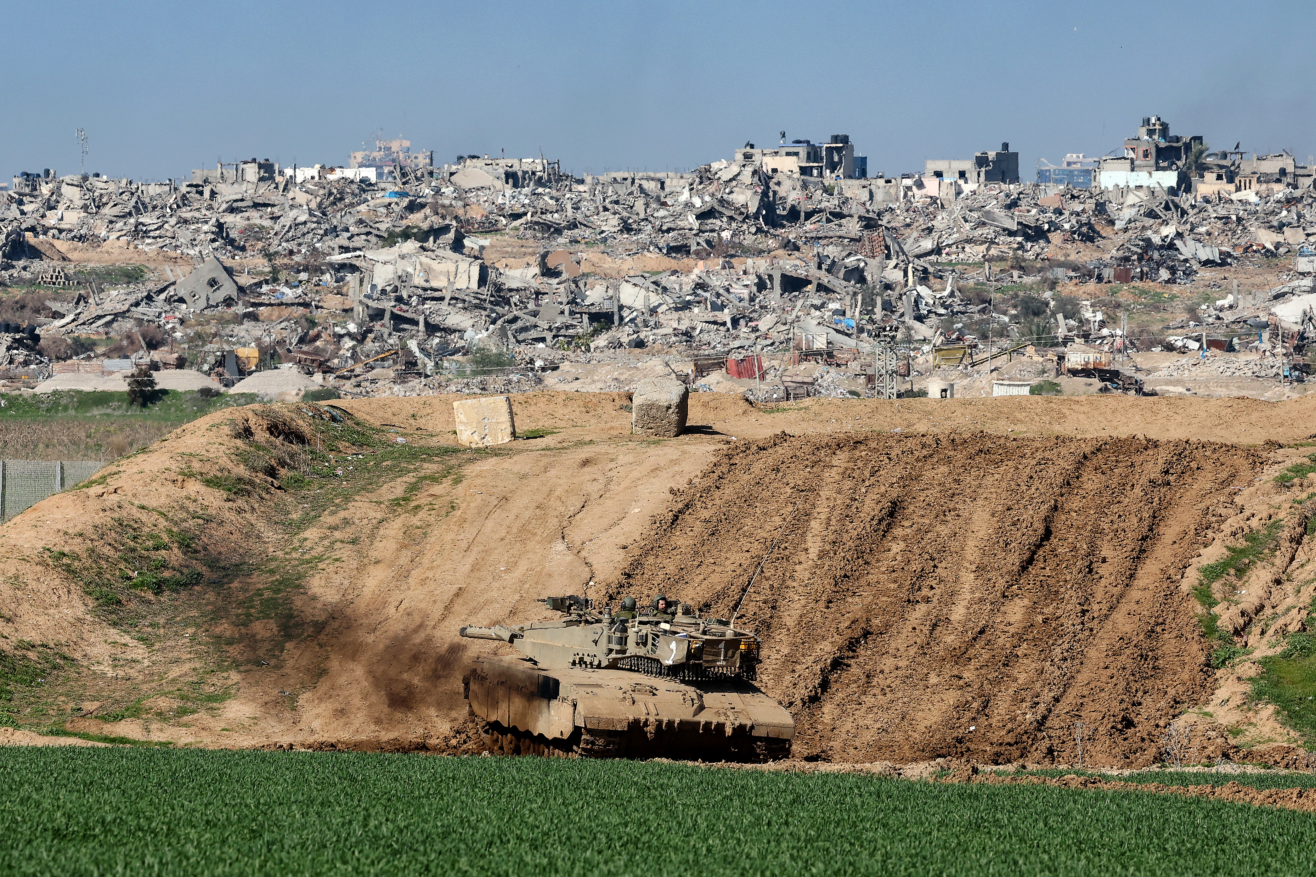 A photo taken from southern Israel, along the border with Gaza, shows an Israeli tank positioned behind a sand wall and damaged buildings in Gaza on January 18. 