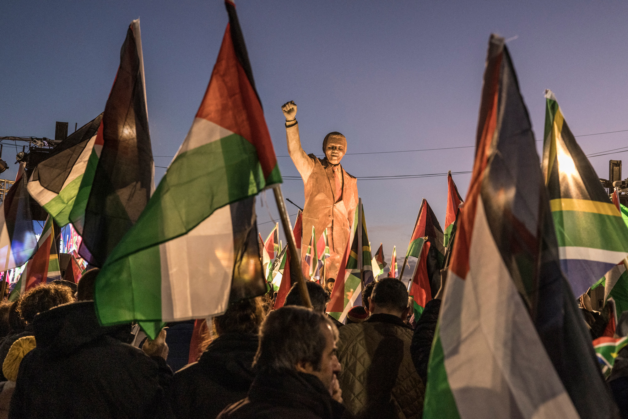 People raise flags and placards as they gather around a statue of late South African president Nelson Mandela to celebrate a landmark genocide case filed by South Africa against Israel at the International Court of Justice, in the occupied West Bank city of Ramallah, on January 10.