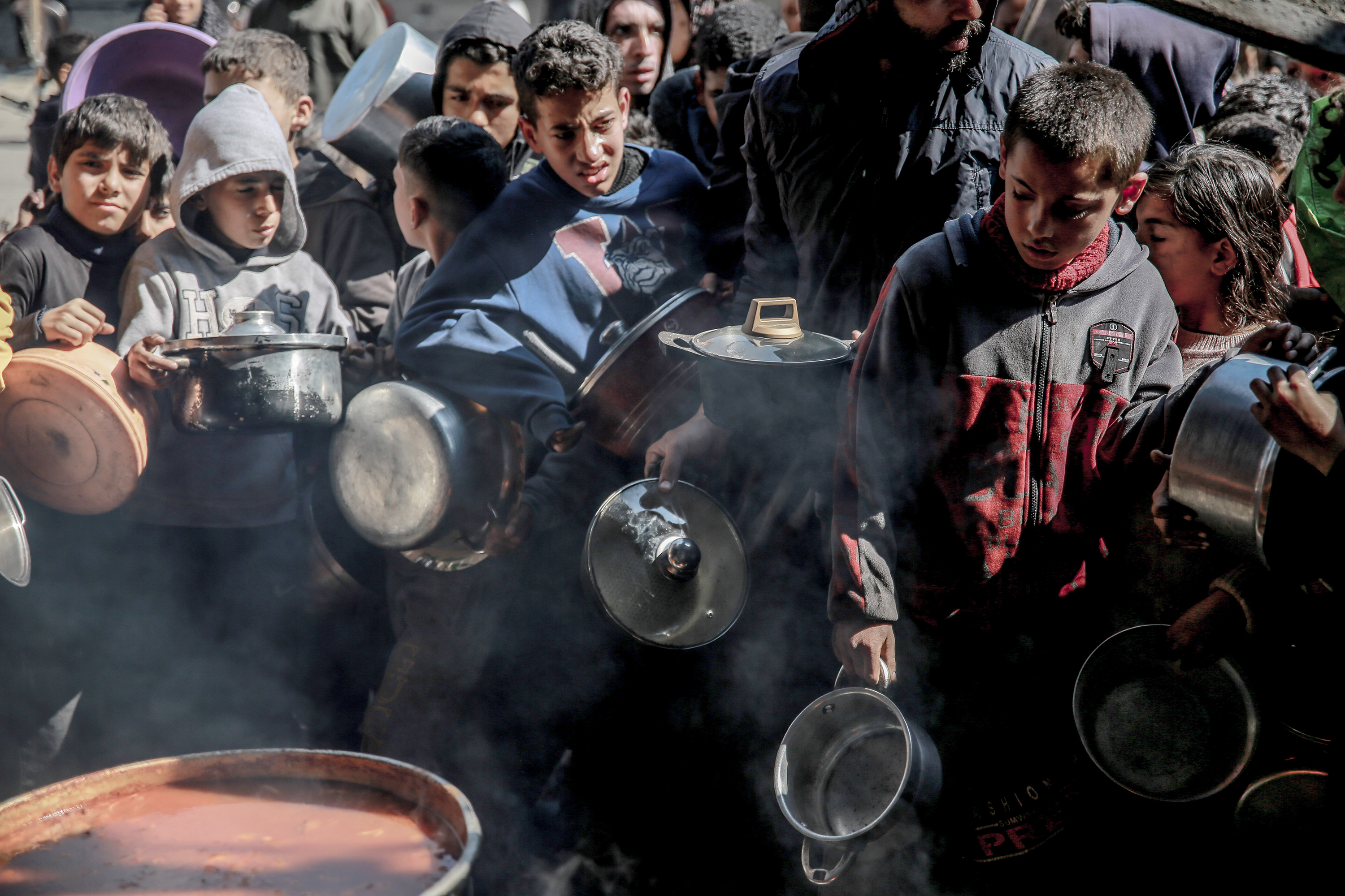 Palestinian Children with empty containers wait in front of boilers to receive hot food in Gaza City on February 26.