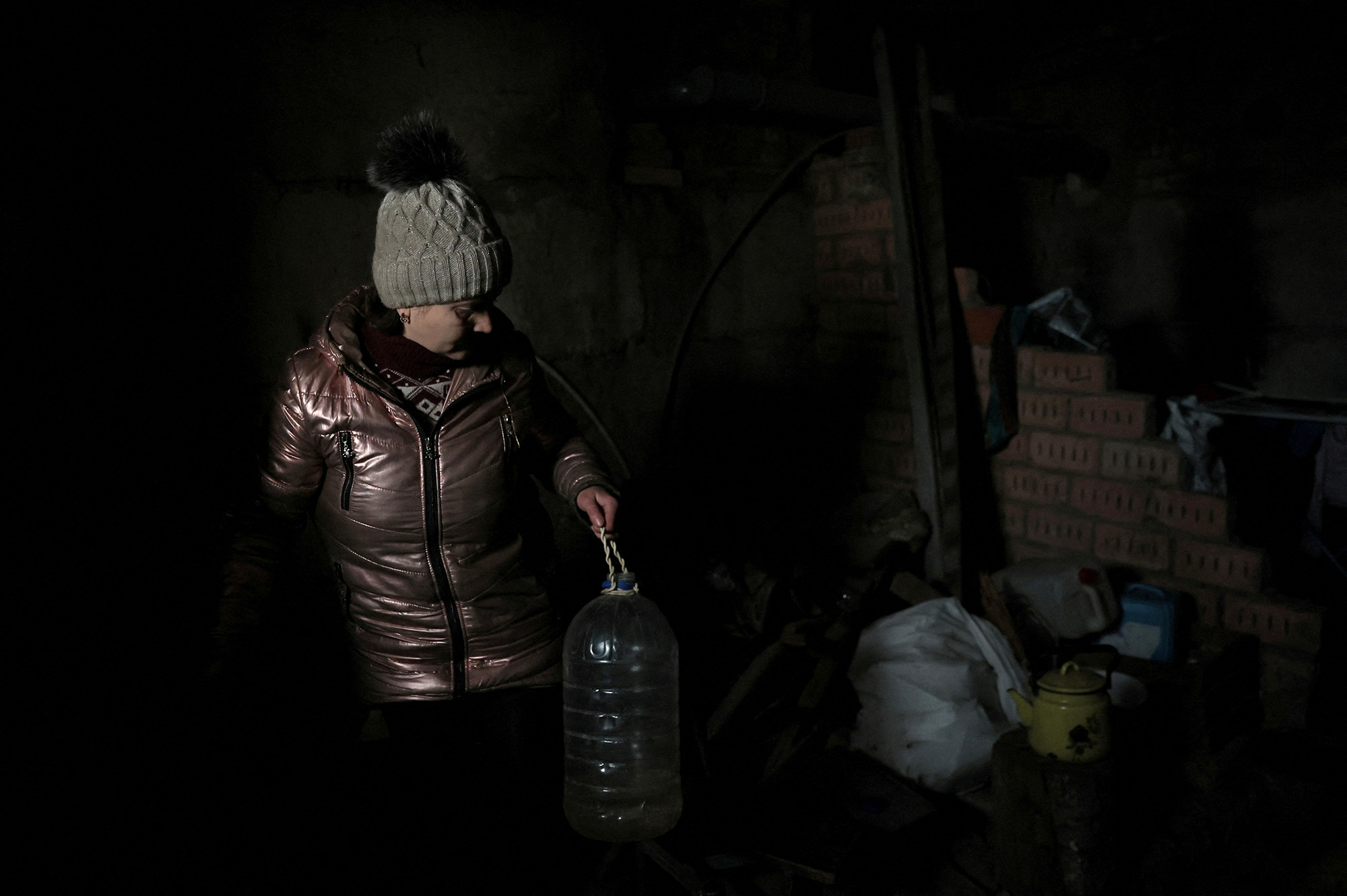 Lilia, 44, pours water into a pot to boil in the basement of an apartment building where she is currently living without power, water or heat in Siversk, Ukraine, on December 4.