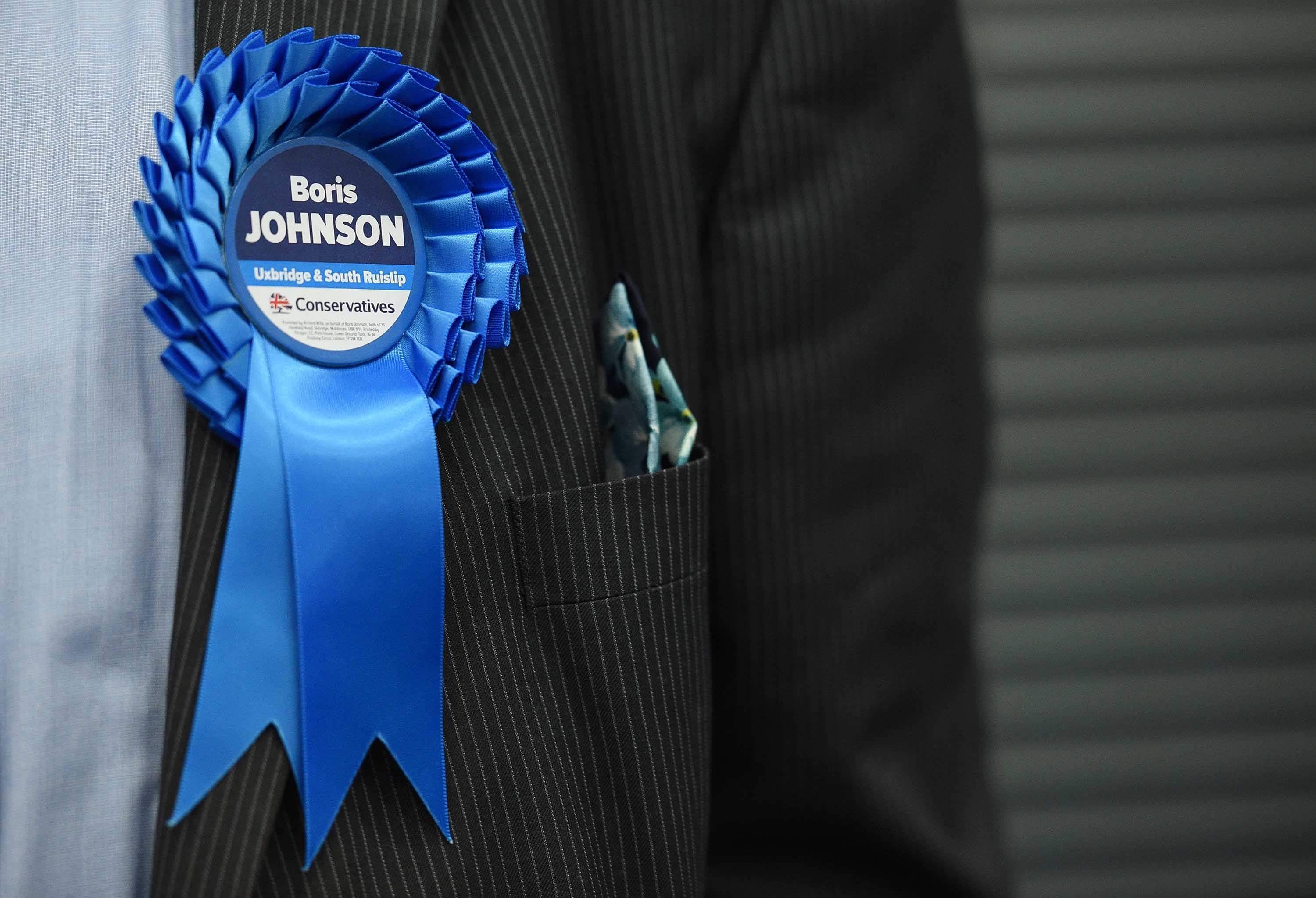 A Conservative Party activist wears a rosette as ballots are tallied in Uxbridge, England. Photo: Oli Scarff/AFP via Getty Images