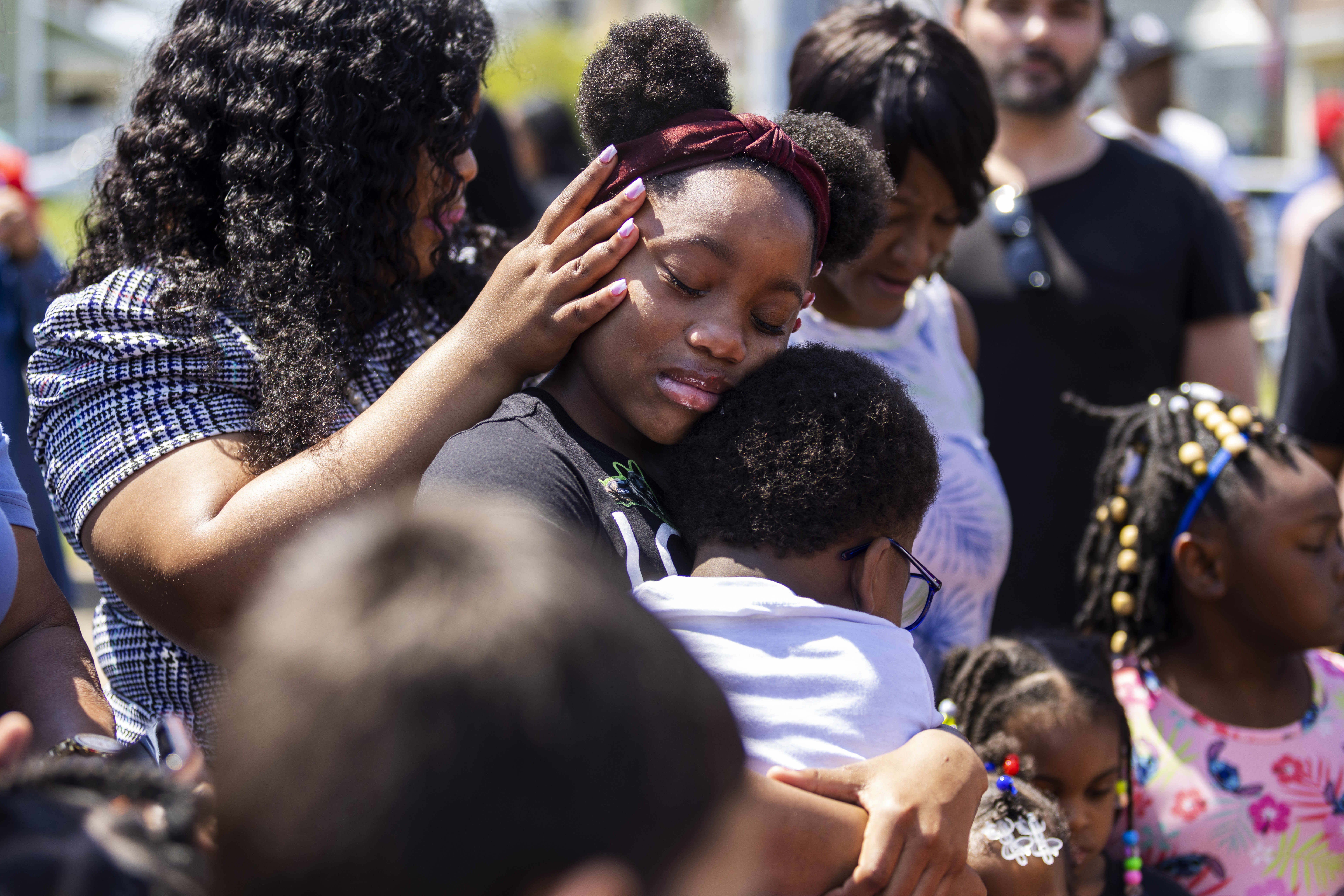 People lay their hands on Deazjah Roseboro, 12, as she comforts her cousin, Jerney Moss, 8, following a mass shooting at a Tops Friendly Market in Buffalo, NY, on Sunday, May 15.