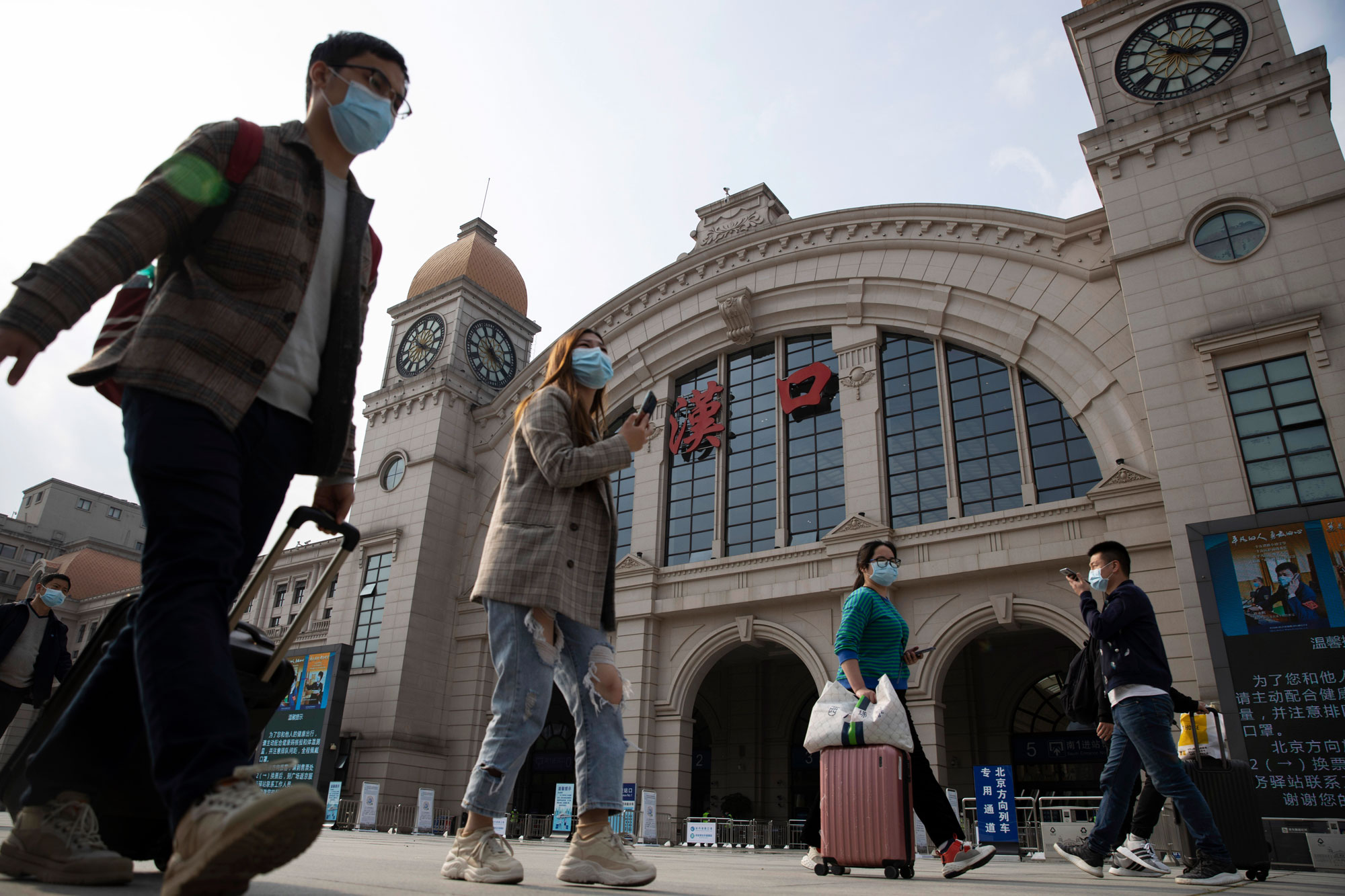 Travelers with their luggage walk past the Hankou railway station on the eve of its resuming outbound traffic in Wuhan in central China's Hubei province on Tuesday, April 7.