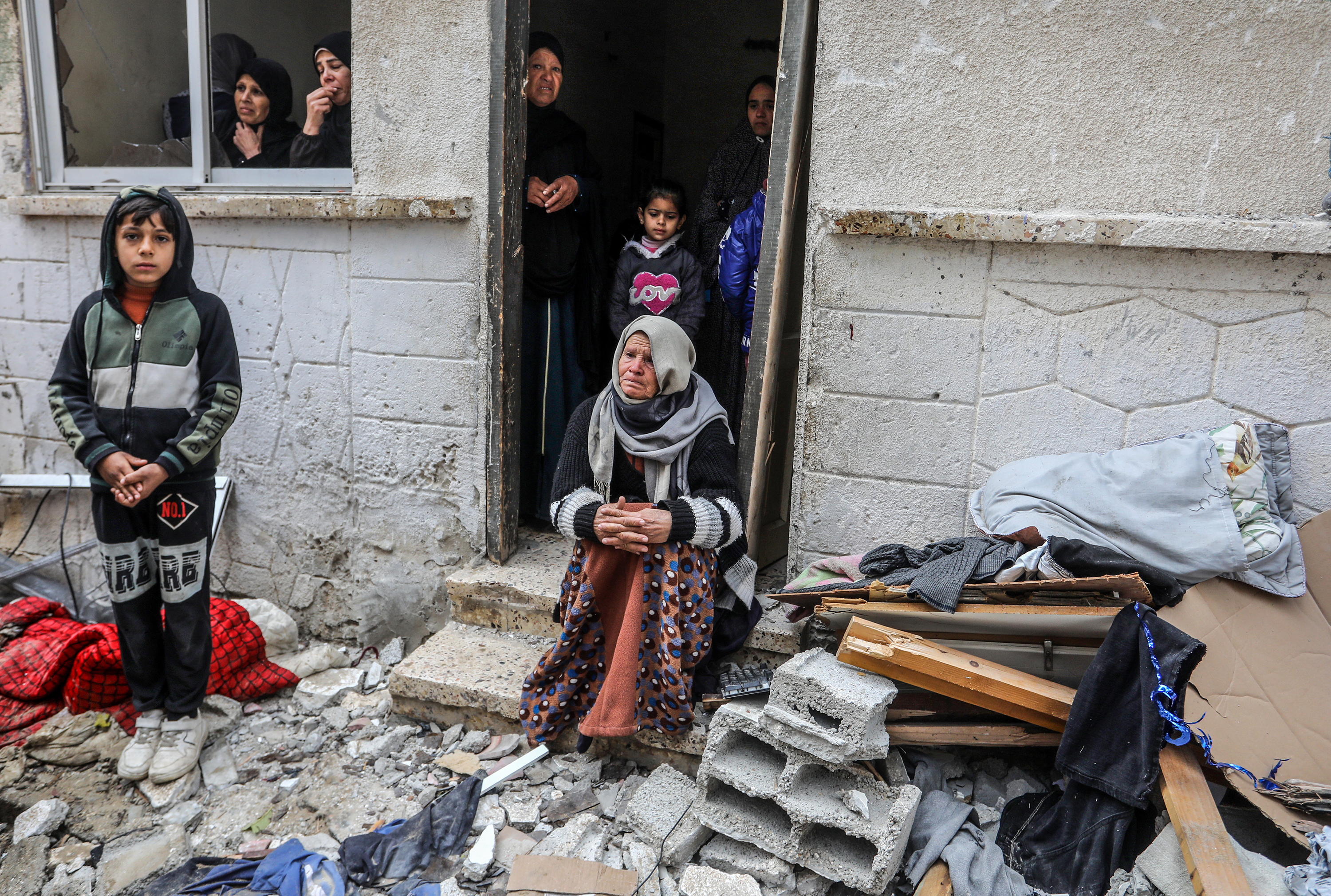 An elderly woman sits at the entrance of a damaged house and Palestinians look at the damaged area after Israeli attacks in Rafah, Gaza on February 9.