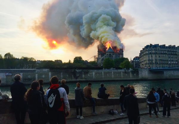 Bystanders look on as flames and smoke billow from the roof.