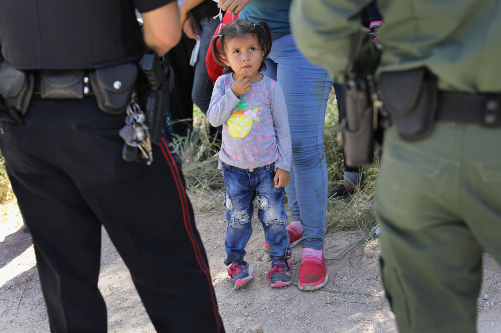 A Mission Police Dept. officer (L), and a U.S. Border Patrol agent watch over a group of Central American asylum seekers before taking them into custody on June 12, 2018 near McAllen, Texas.