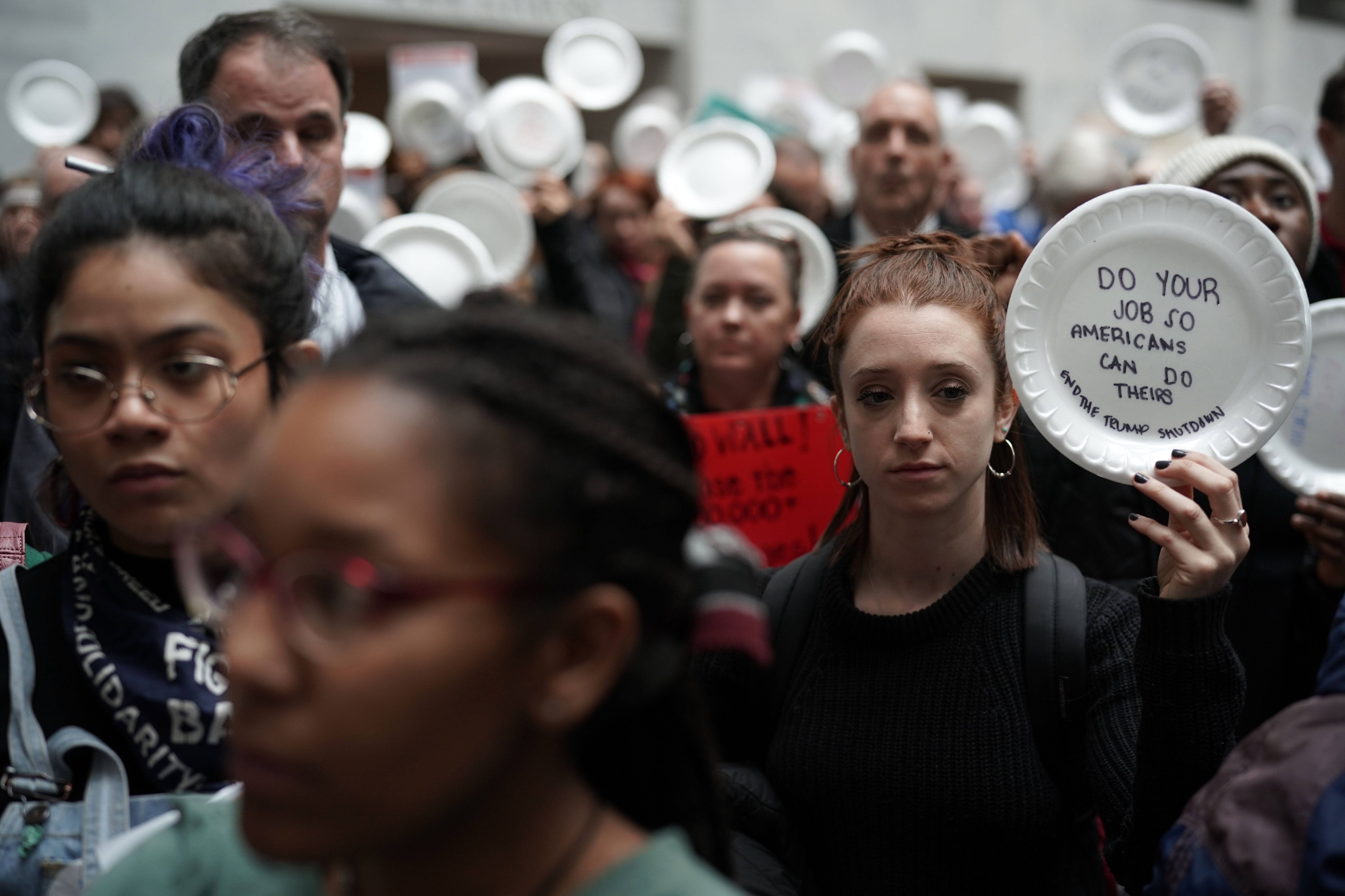 Federal employees hold up signs made with styrofoam plates during a protest at the atrium of Senate Hart Office Building.