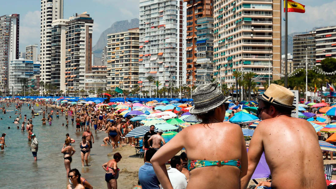 Beach-goers cool off and sunbathe on the beach of the seaside resort of Benidorm, on August 5, 2018 - Europe sweltered through an intense heatwave today, with soaring temperatures contributing to forest fires, nuclear plants closing and even threatening the Netherlands' supply of fries, although some countries experienced a slight respite. (Photo by JOSE JORDAN / AFP)        (Photo credit should read JOSE JORDAN/AFP via Getty Images)