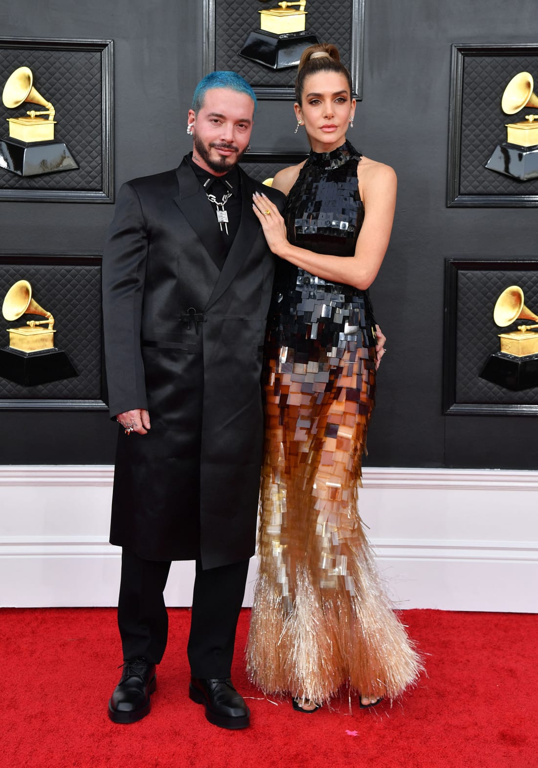 J Balvin elevated the suit silhouette in a tailored knee-length coat, while model Valentina Ferrer opted for a high-neck layered ombre dress with a gold fringed hem. 