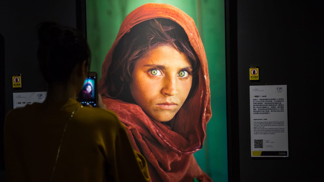 A visitor takes photos of a 1985 National Geographic magazine cover "Afghan Girl" Sharbat Gula displayed at the National Geographic Exhibition in September 2017.