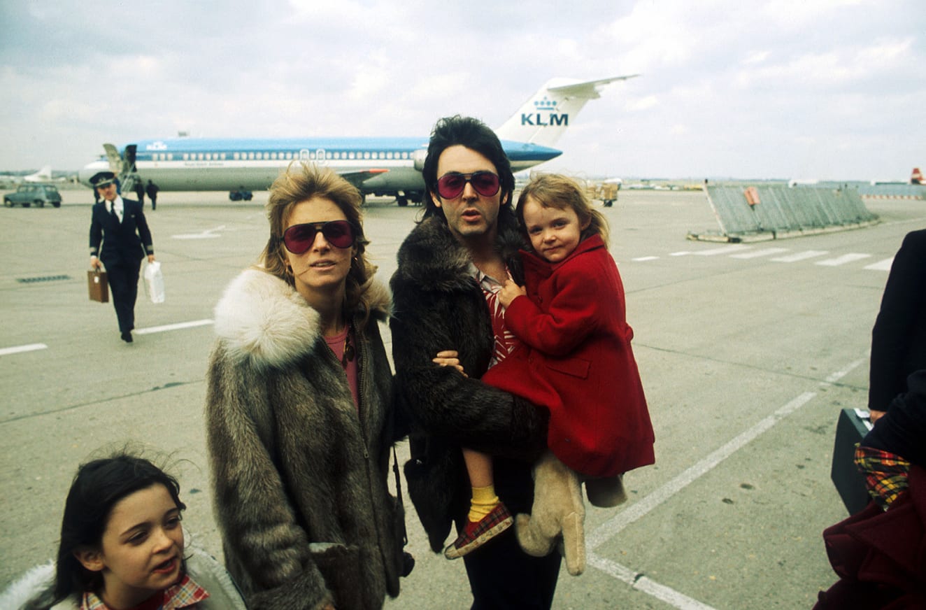 A young Stella McCartney is carried by her father, who dons a pair of sunglasses at an airport in 1988.