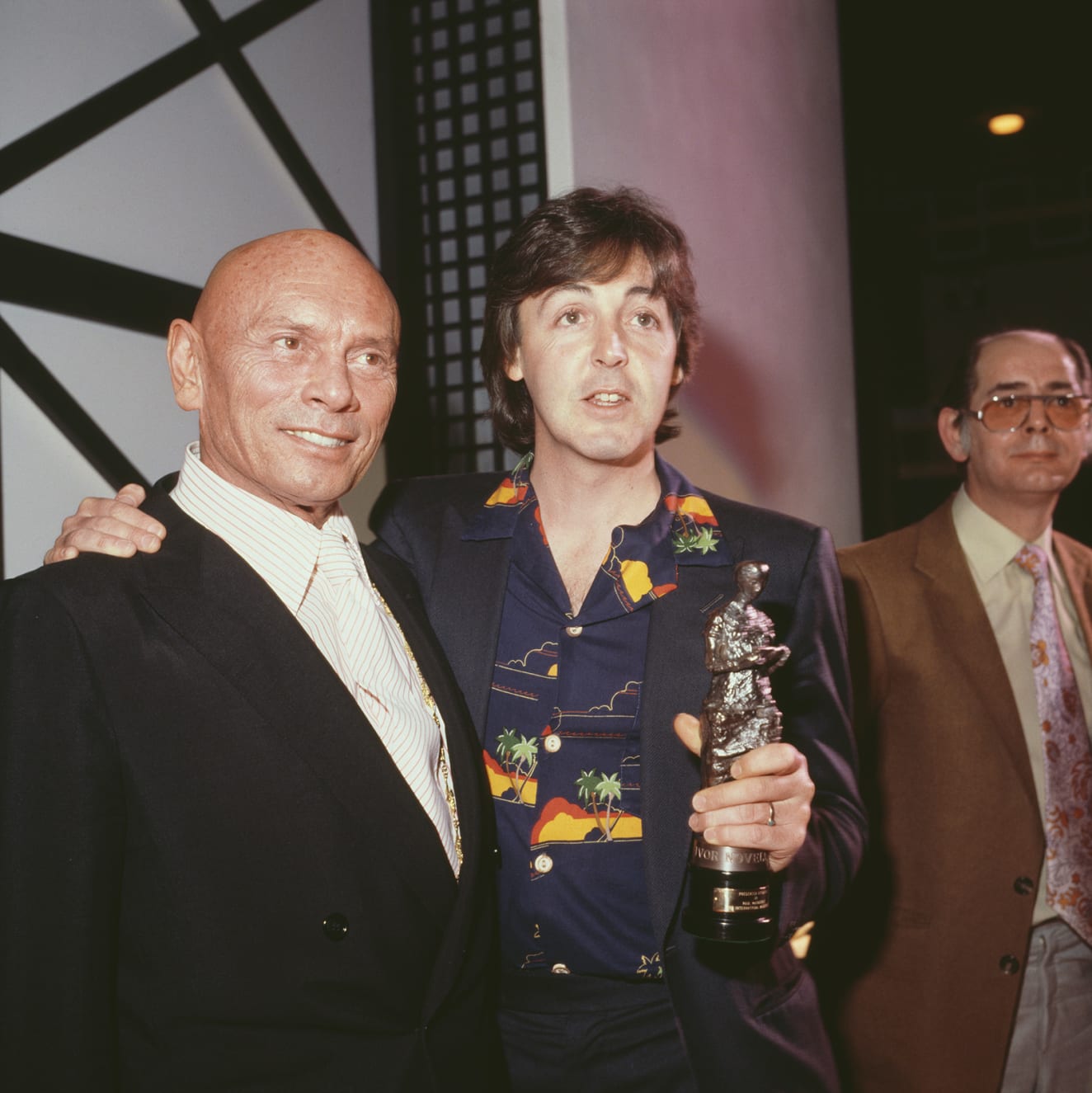 Always playful, McCartney styled a Hawaiian shirt and blazer to collect his Ivor Novello award at Grosvenor House in London from Russian-born actor Yul Brynner in 1980.