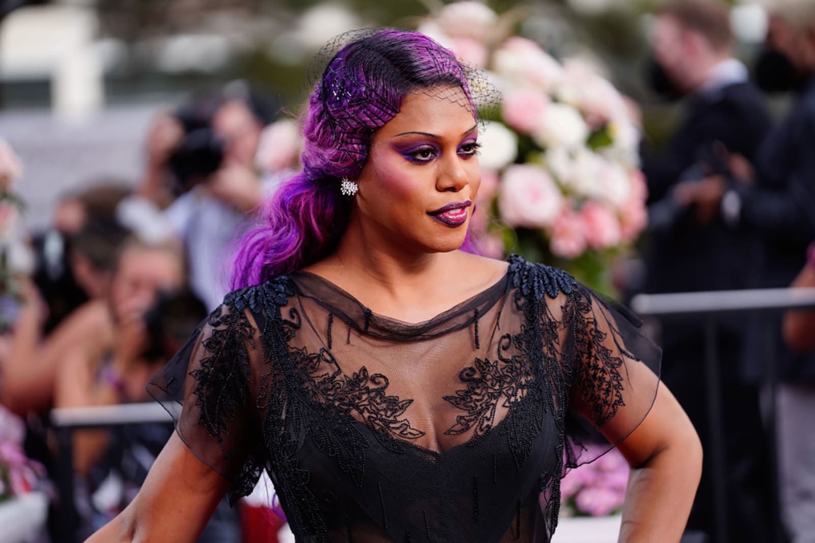 Laverne Cox in a black John Galliano dress, purple hair and dark makeup. 