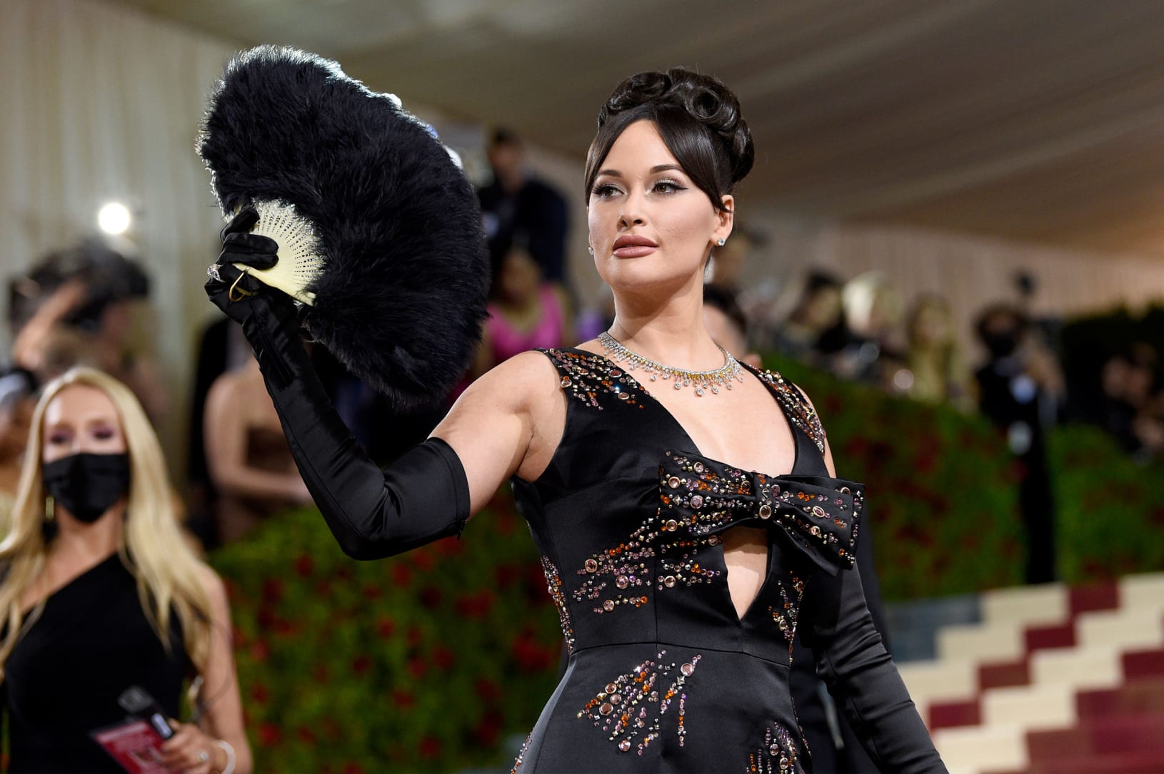 Musician Kacey Musgraves arrived with an oversized feathered fan, wearing an embellished low-cut black Prada dress with a front bow.