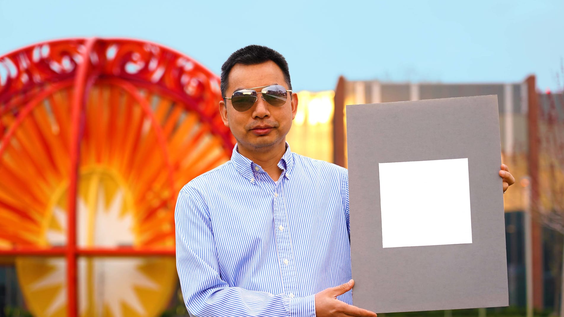 Xiulin Ruan, a Purdue University professor of mechanical engineering, poses with a sample of the new, sunlight reflecting paint.