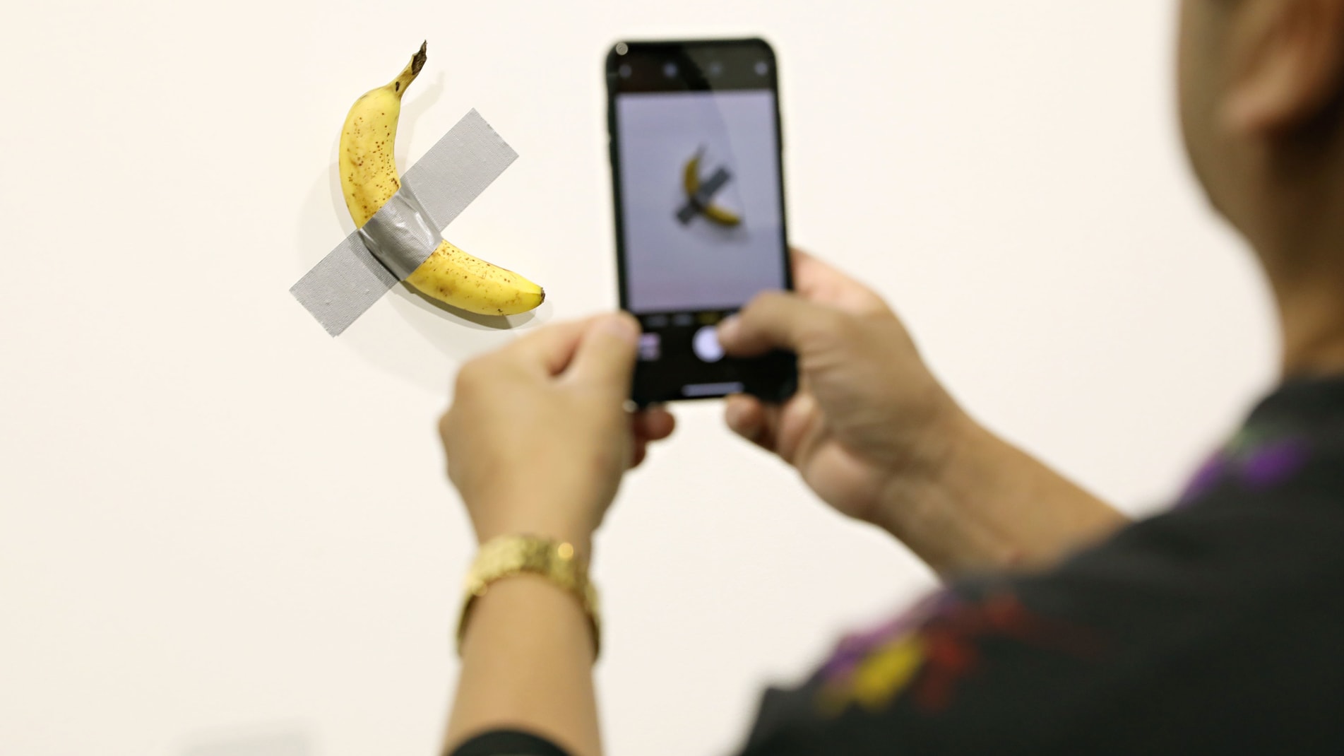 MIAMI BEACH, FL - DECEMBER 06:  People post in front of Maurizio Cattelan's "Comedian" presented by Perrotin Gallery and on view at Art Basel Miami 2019 at Miami Beach Convention Center on December 6, 2019 in Miami Beach, Florida. Two of the three editions of the piece, which feature a banana duct-taped to a wall, have reportedly sold for $120,000.  (Photo by Cindy Ord/Getty Images)