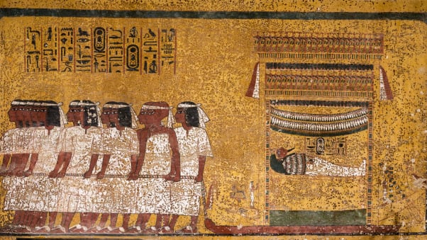 East wall of the tomb's burial chamber. Tutankhamun's mummy is shown, lying in a shrine mounted on a sledge, being drawn by 12 men in ﬁve groups. The men wear white mourning bands over their brows. The last pair, distinguished by their shaven heads and different dress, are the two viziers of Upper and Lower Egypt.