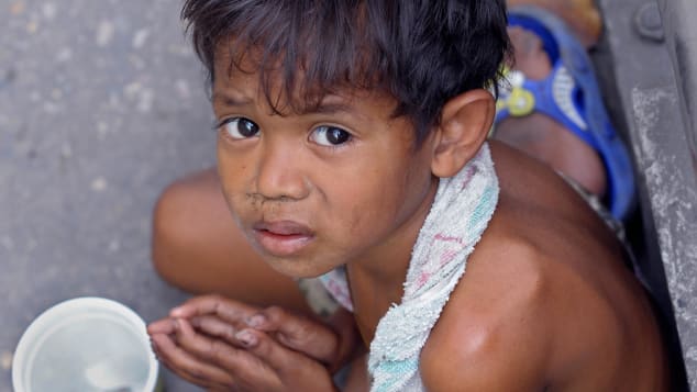 A Thai boy begs for money along a streetside pavement in Bangkok.