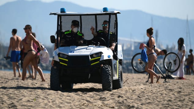 Spanish policemen ask people that were sunbathing to leave the Barceloneta beach in Barcelona on May 20, 2020 during the hours allowed by the government to exercise.