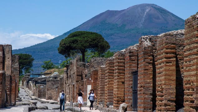 Visitors walk across the archeological site of Pompeii at the bottom of the Mount Vesuvius volcano (Rear) on May 26, 2020, as the country eases its lockdown aimed at curbing the spread of the COVID-19 infection, caused by the novel coronavirus. - Italy's world-famous archeological site Pompeii reopened to the public on May 26,bBut with foreign tourists still prohibited from travel to Italy until June, the site that attracted just under 4 million visitors in 2019 is hoping that for now, Italian tourists can make up at least a fraction of the difference. (Photo by Tiziana FABI / AFP) (Photo by TIZIANA FABI/AFP via Getty Images)