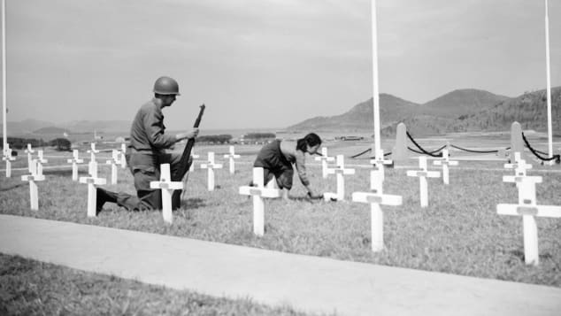 An American corporal watches as a 9-year-old Korean girl places a bouquet of white roses on the grave of one of his fallen comrades at a UN memorial near Busan, South Korea, in 1951.