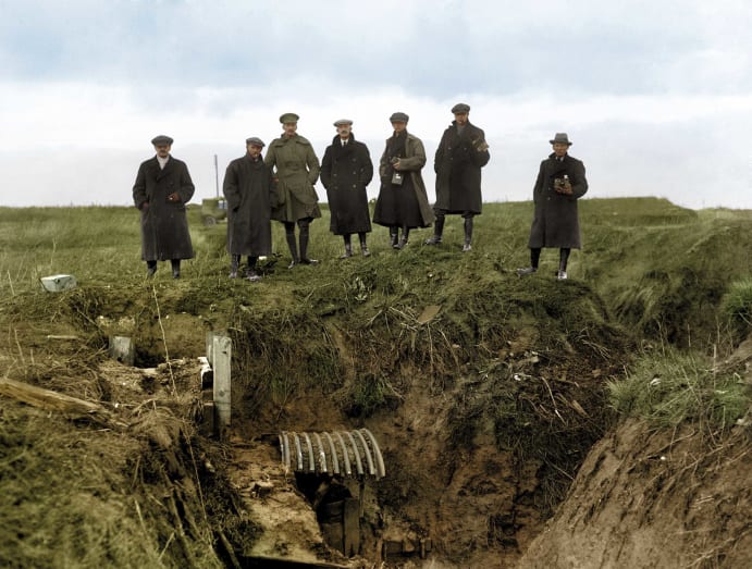 Journalists look down into a First World War trench.