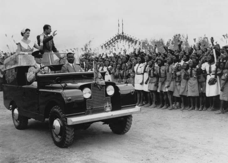 Queen Elizabeth II and Prince Philip wave from an open Land Rover in Ibadan, Nigeria, 1956.