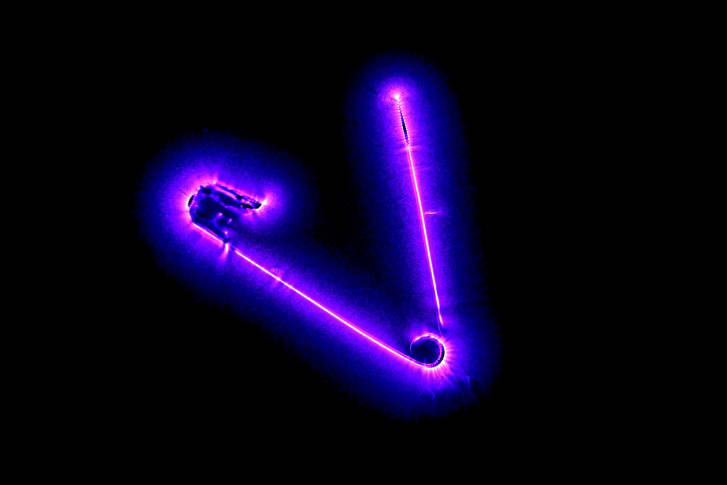 Safety Corona by Richard Germain. A safety pin is connected to a high tension AC generator. The pin ionizes the air around it. When the electrons fall back on an atom, the excess energy is emitted as a photon, which generate the corona glow around the pin. The fuzziness of the pin is because the camera did not actually capture light reflected on the pin but rather the light emitted by the ionized light around it.  