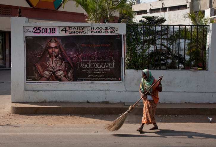 An Indian municipal worker sweeps a street in front of a poster of Bollywood film "Padmaavat" outside a movie theatre in Hyderabad, India in 2018.